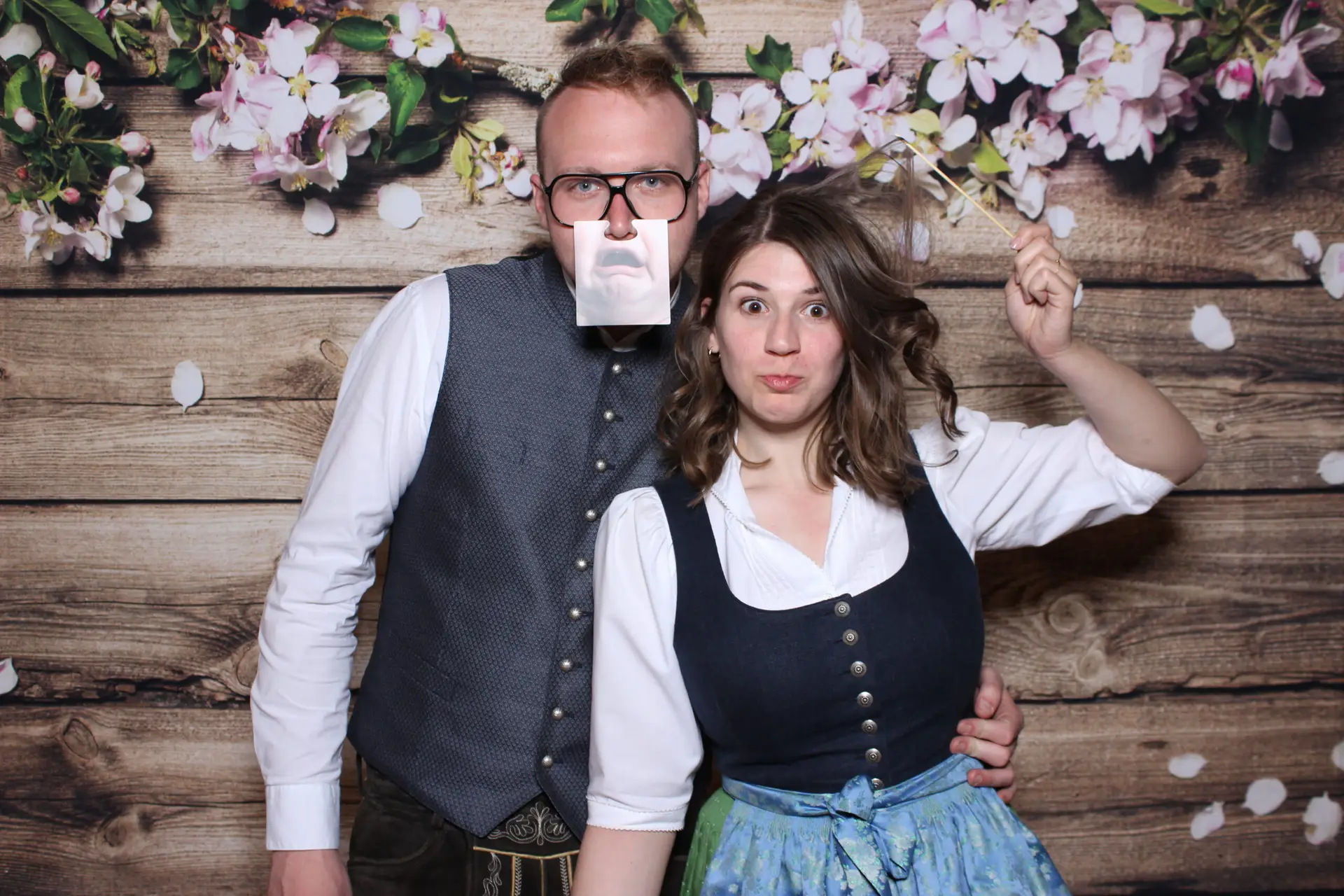 Hochzeitsgäste in Tracht posieren vor einem floralen Fotobox-Hintergrund