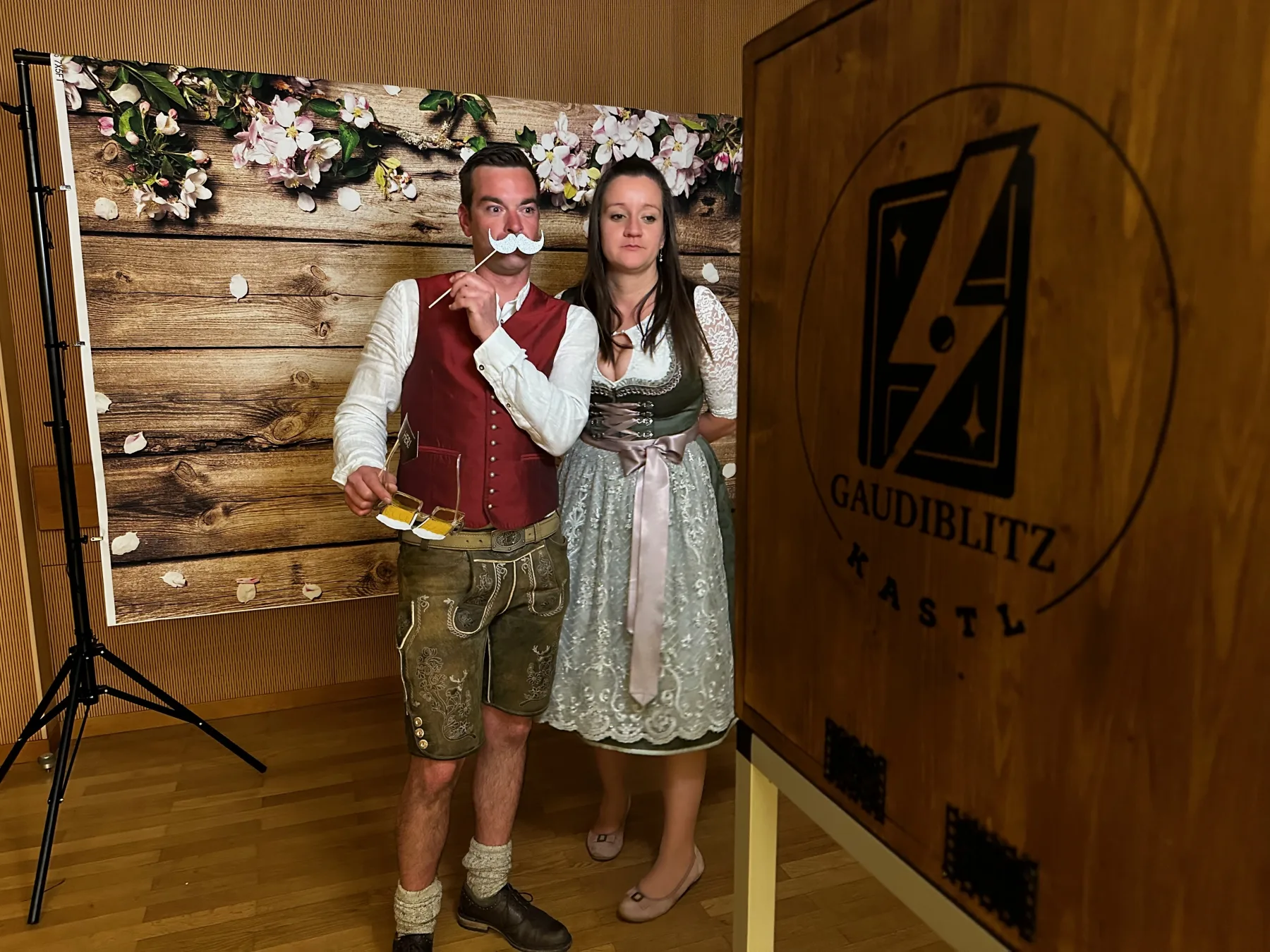 Gäste in Tracht posieren mit Requisiten vor der GaudiBlitzKastl Fotobox bei einem Ballabend