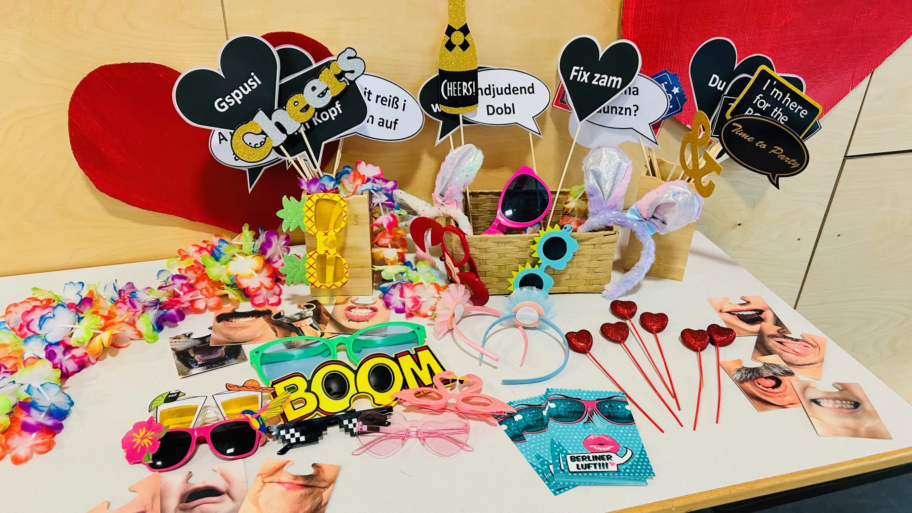 Auswahl an bunten Fotobox-Requisiten mit Brillen, Schildern und Accessoires auf einem Tisch